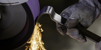 worker grinding a tool using 3M Cubitron 3 belts