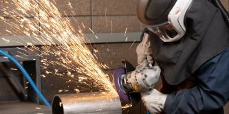 worker wearing welding helmet grinding metal