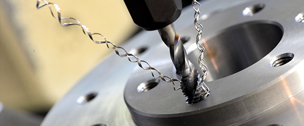 Close-up view of a machine tap cutting internal threads into a metal component, with spiral metal chips forming as the tool rotates